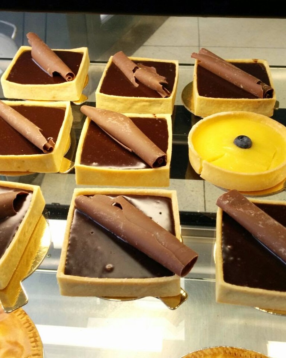 Individual chocolate tarts with chocolate curls and a lemon tart in the display case at Baker Street Bakery