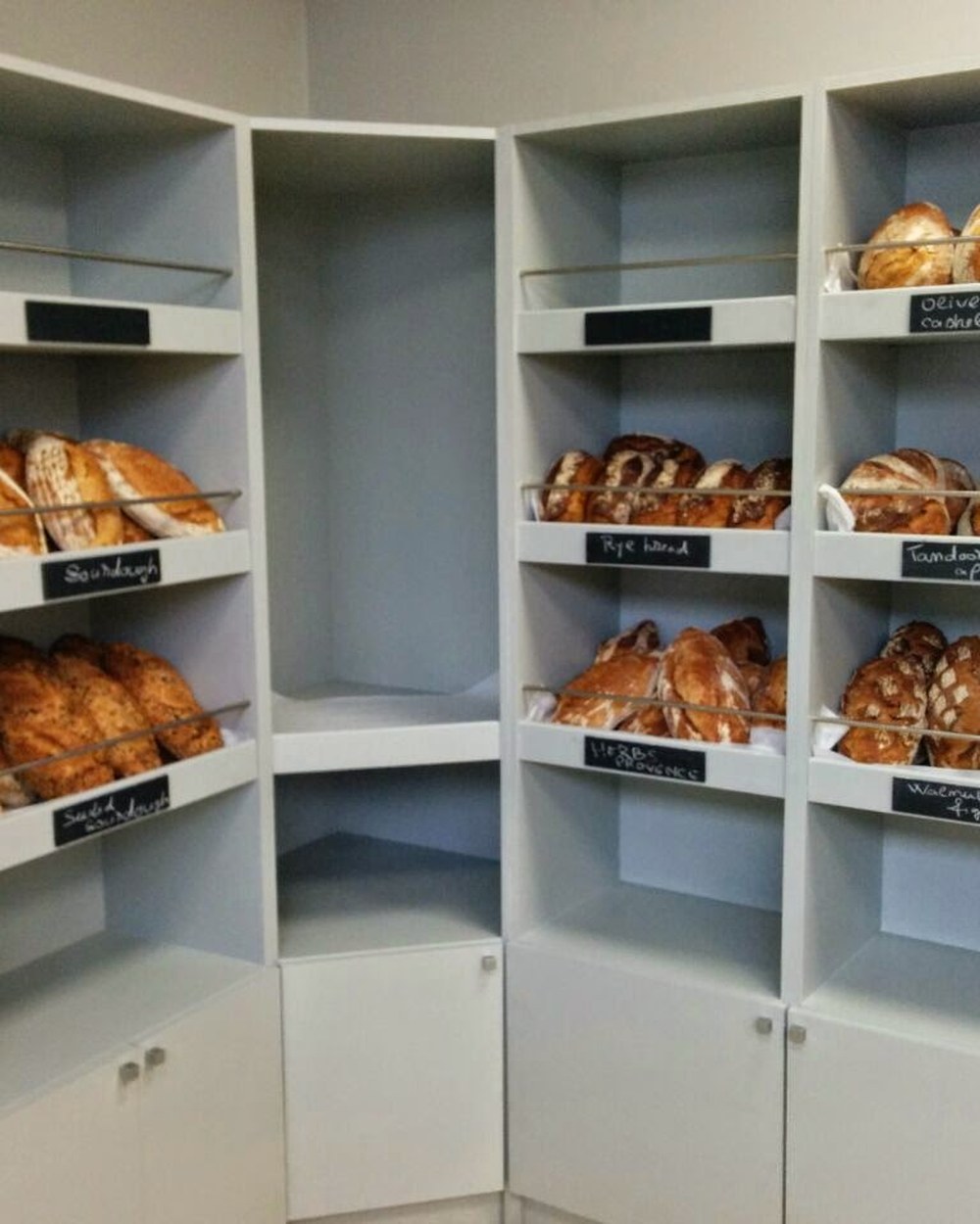 Shelves of sourdough and rye loaves with hand-chalked labels at Baker Street Bakery